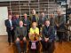 Carol Conlin, seated, holding flowers, surrounded by the Governors and Guardians of Armagh Robinson Library in the Library's Long Room.