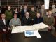 Ten people standing and seated behind a table in an historic library, with an open copy of the 1776 American Atlas in front of them