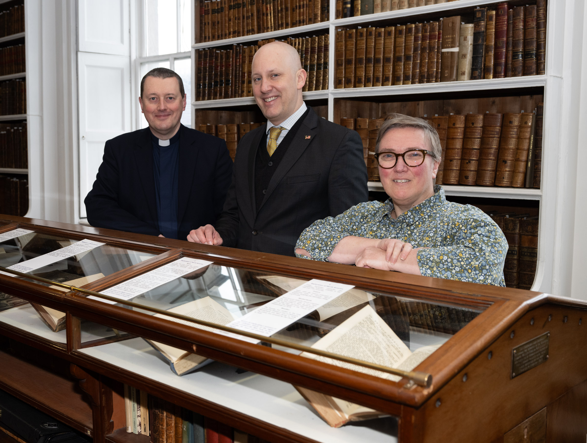 Three people, the keeper of the Library, the US Consul general and the Archivist, standing behind a classic wooden glass-topped display cabinet. Inside the cabinet are open books, which are part of the exhibition United Stated of America: the road to independence.