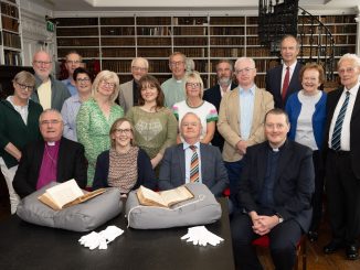 A group of people posing in a historic Library, with the two volumes of the first edition of Gulliver's travels set out on the table in front of them.